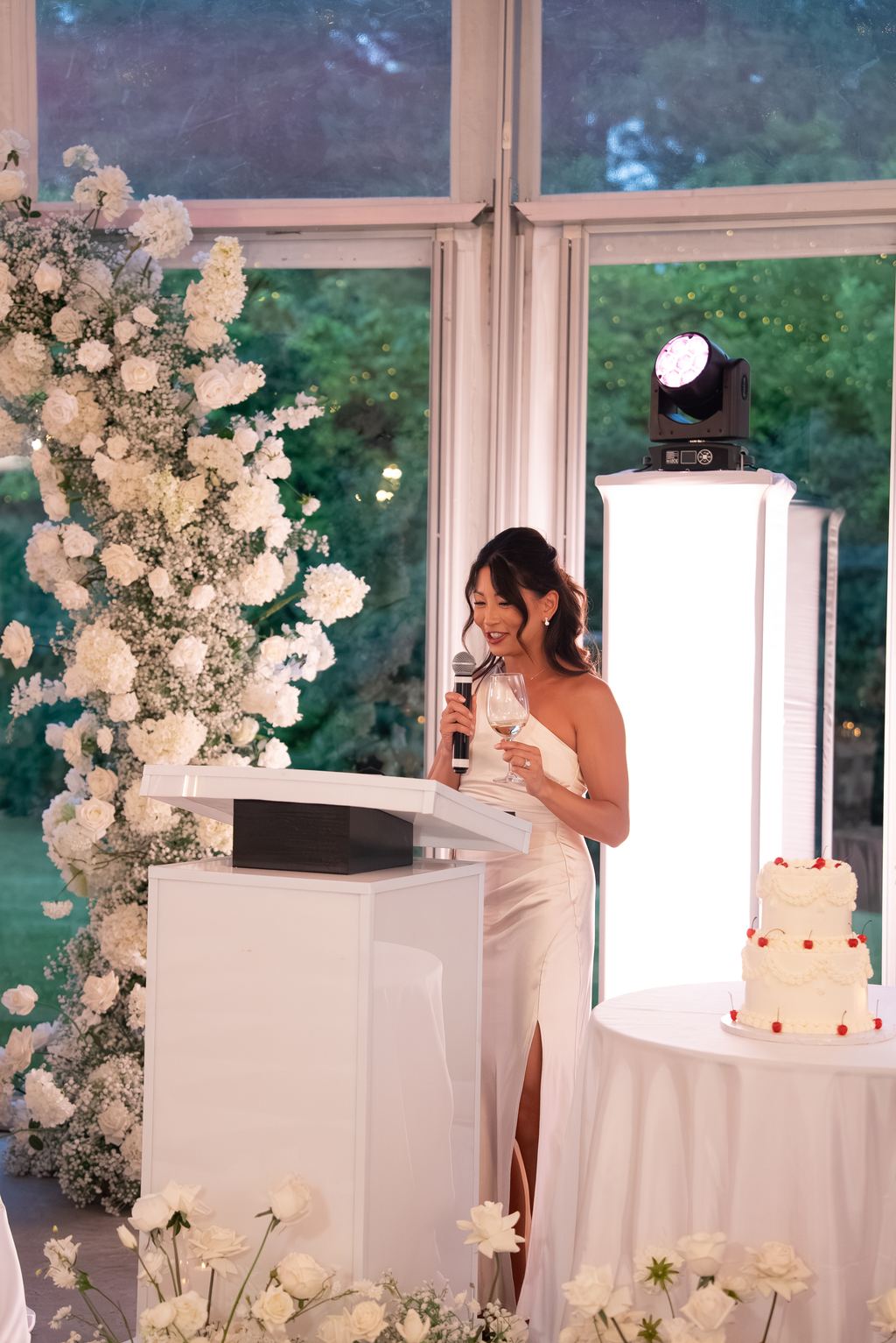 A speaker addressing the room from a podium beside a floral installation