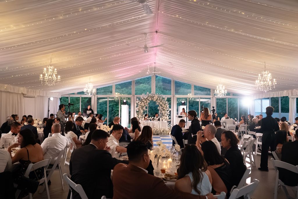 Reception tent lit with chandeliers, string lights and uplighting, guests seated at dinner