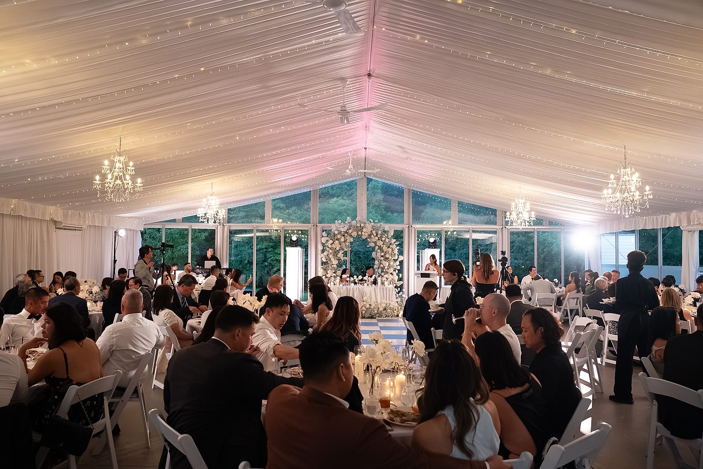 Reception tent lit with chandeliers, string lights and uplighting, guests seated at dinner
