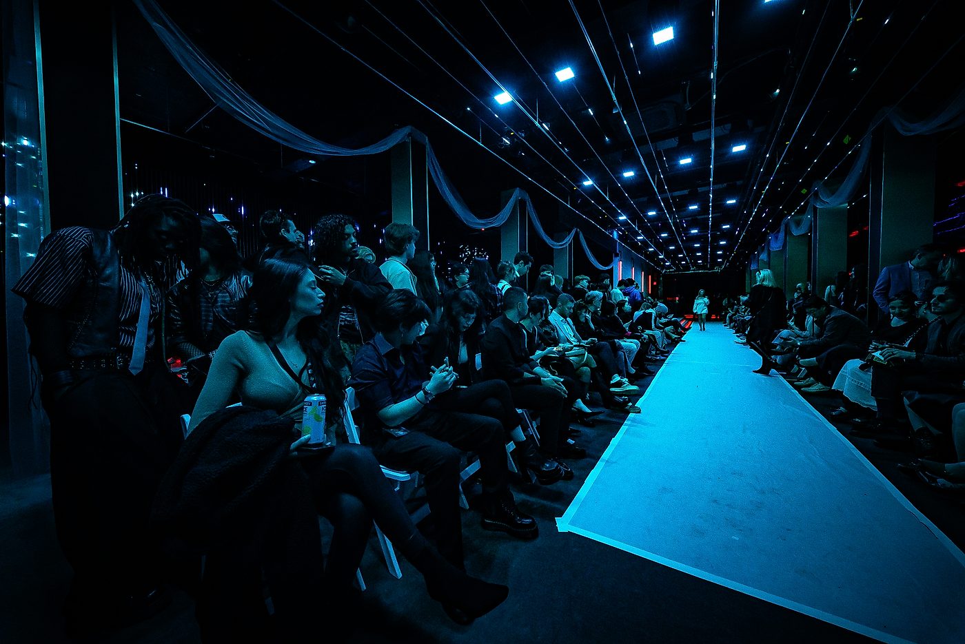 Guests seated along a lit runway under dramatic blue overhead lighting